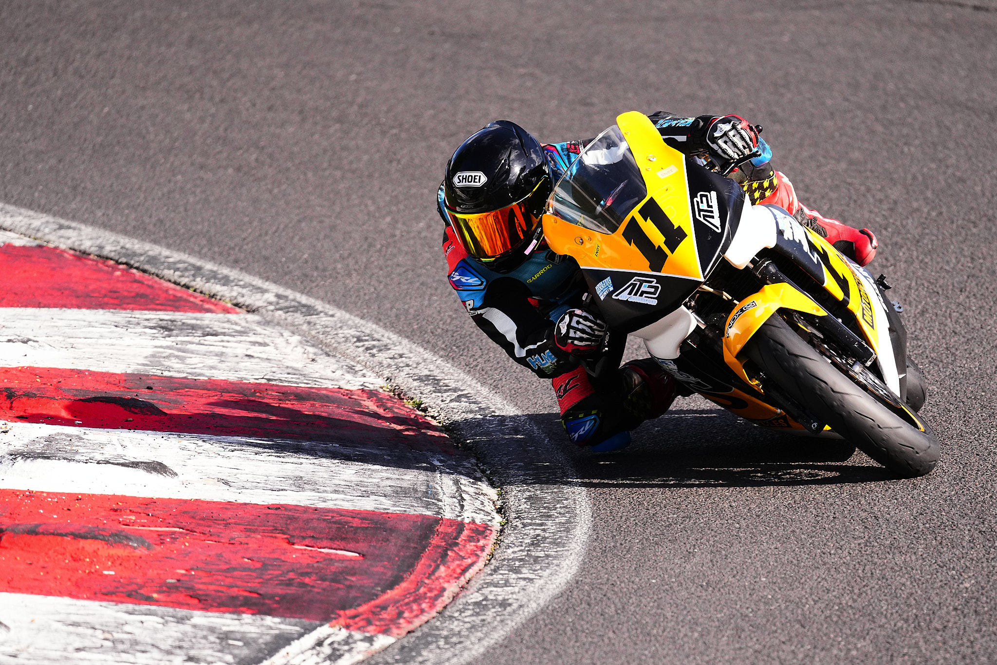 Rider on a yellow and black number 11 sports bike, knee down past red-and-white kerbs at Brands Hatch